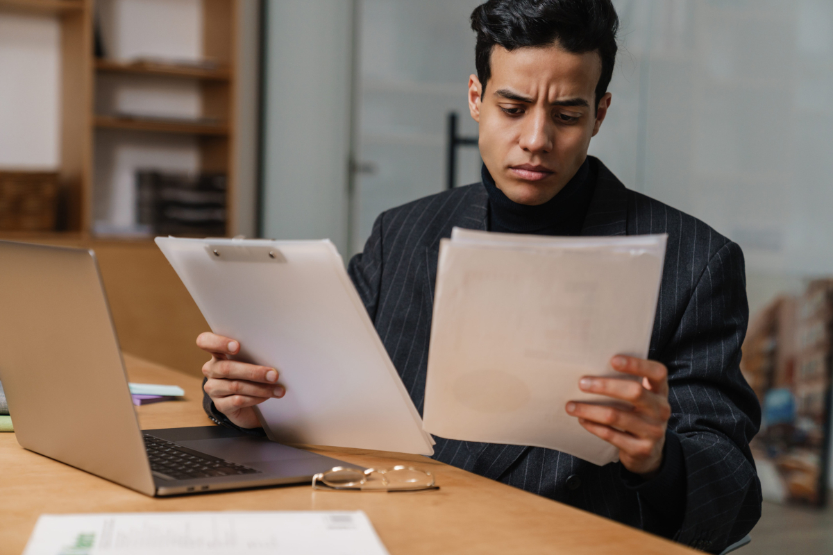 Business owner reviewing paperwork and a laptop at his desk